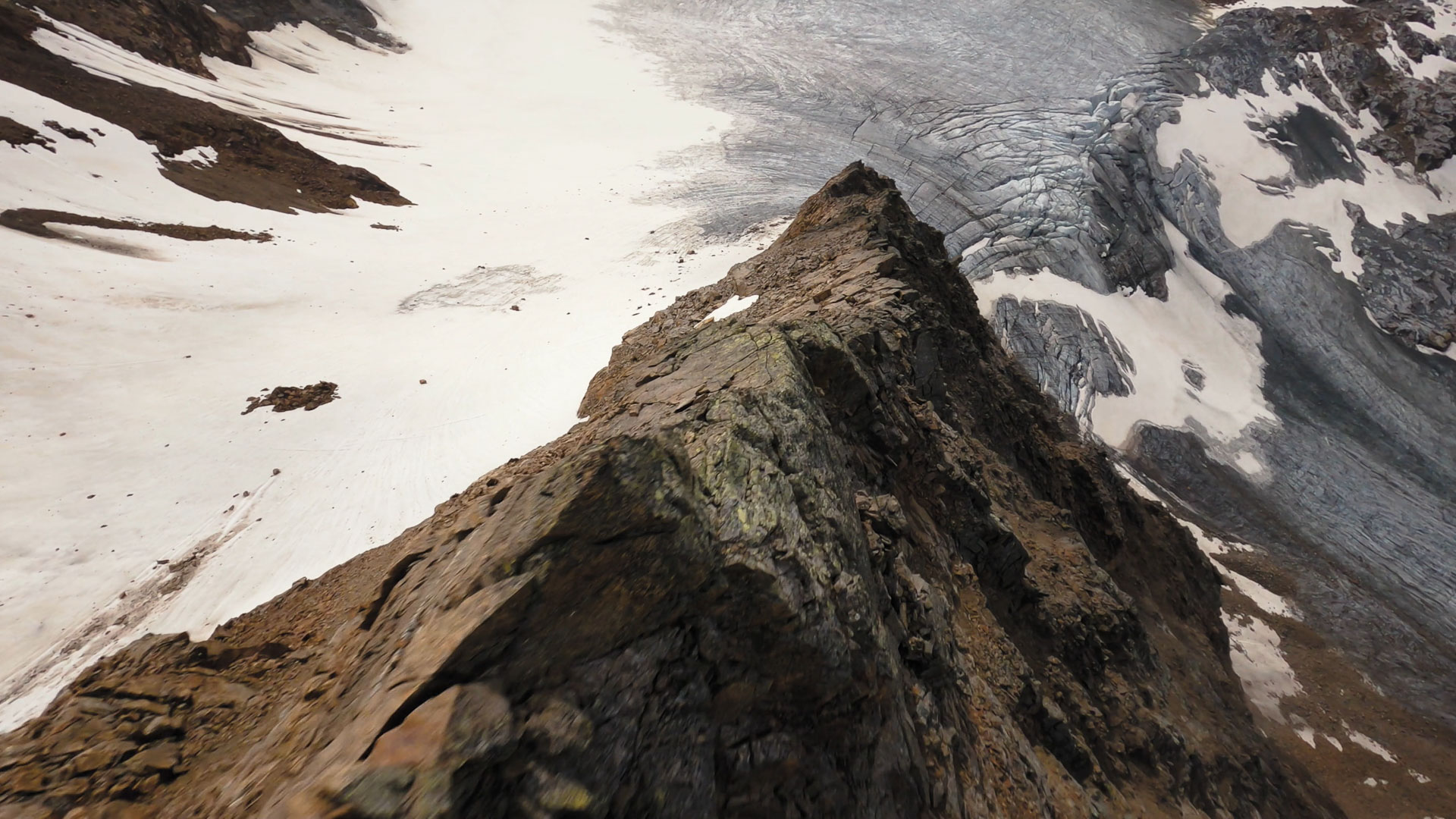 Eine FPV-Drohne fliegt einen steinigen, alpinen Bergkamm hinab Richtung Gletscher, Alpeiner Ferner.