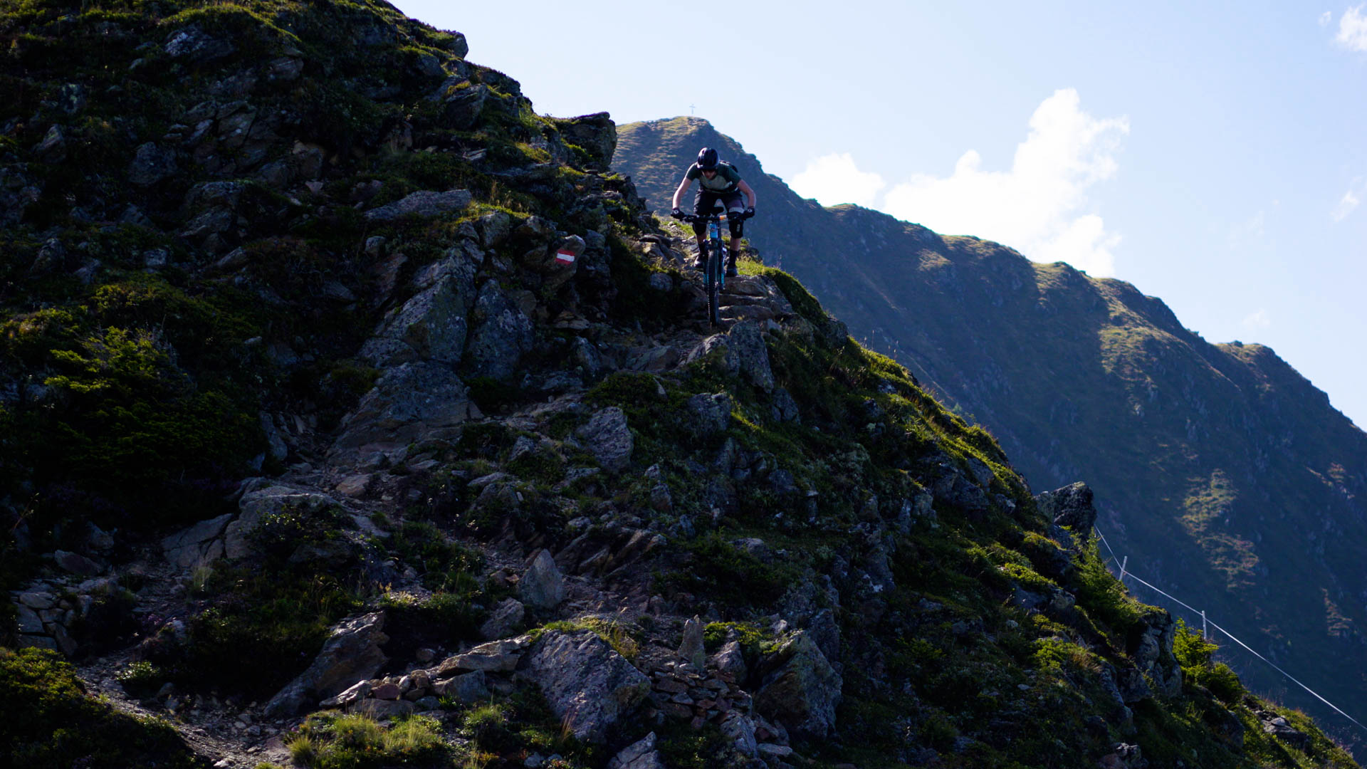 Eine Mountainbikerin auf einem steilen, ausgesetzten, alpinen Trail in den Tiroler Bergen.