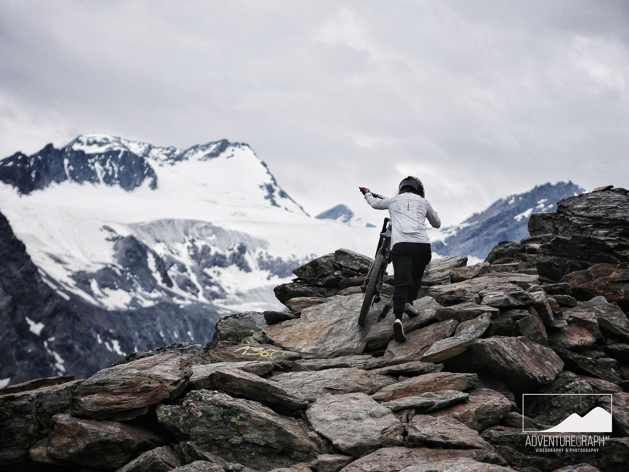 Atmospheric photo of enduro girl pushing her bike through harsh terrain near glacier in Tirol.